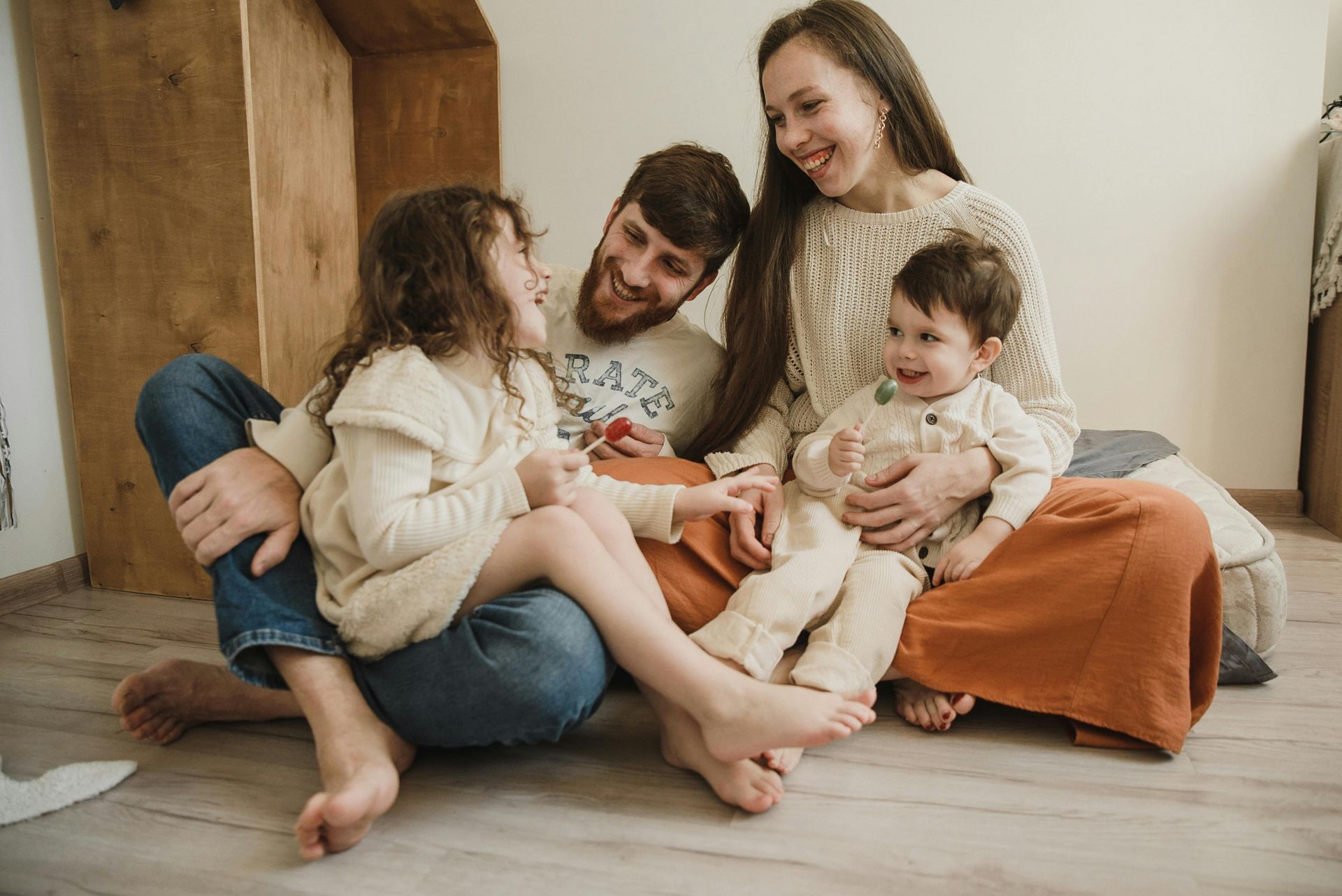 Family sitting on the floor, smiling and cuddling with a baby in a cozy living room.