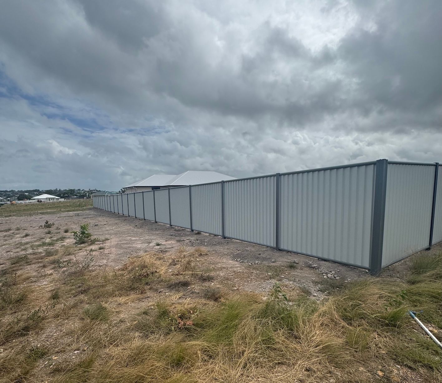 Gray corrugated aluminium fence in a grassy field under a cloudy sky — We Do Fencing in Sunshine Acres, QLD