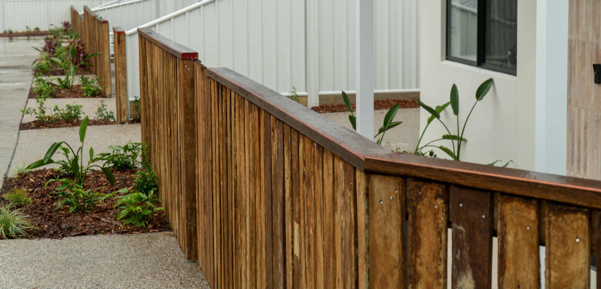 Wooden fence with plants and sidewalk leading to a building— We Do Fencing in Sunshine Acres, QLD