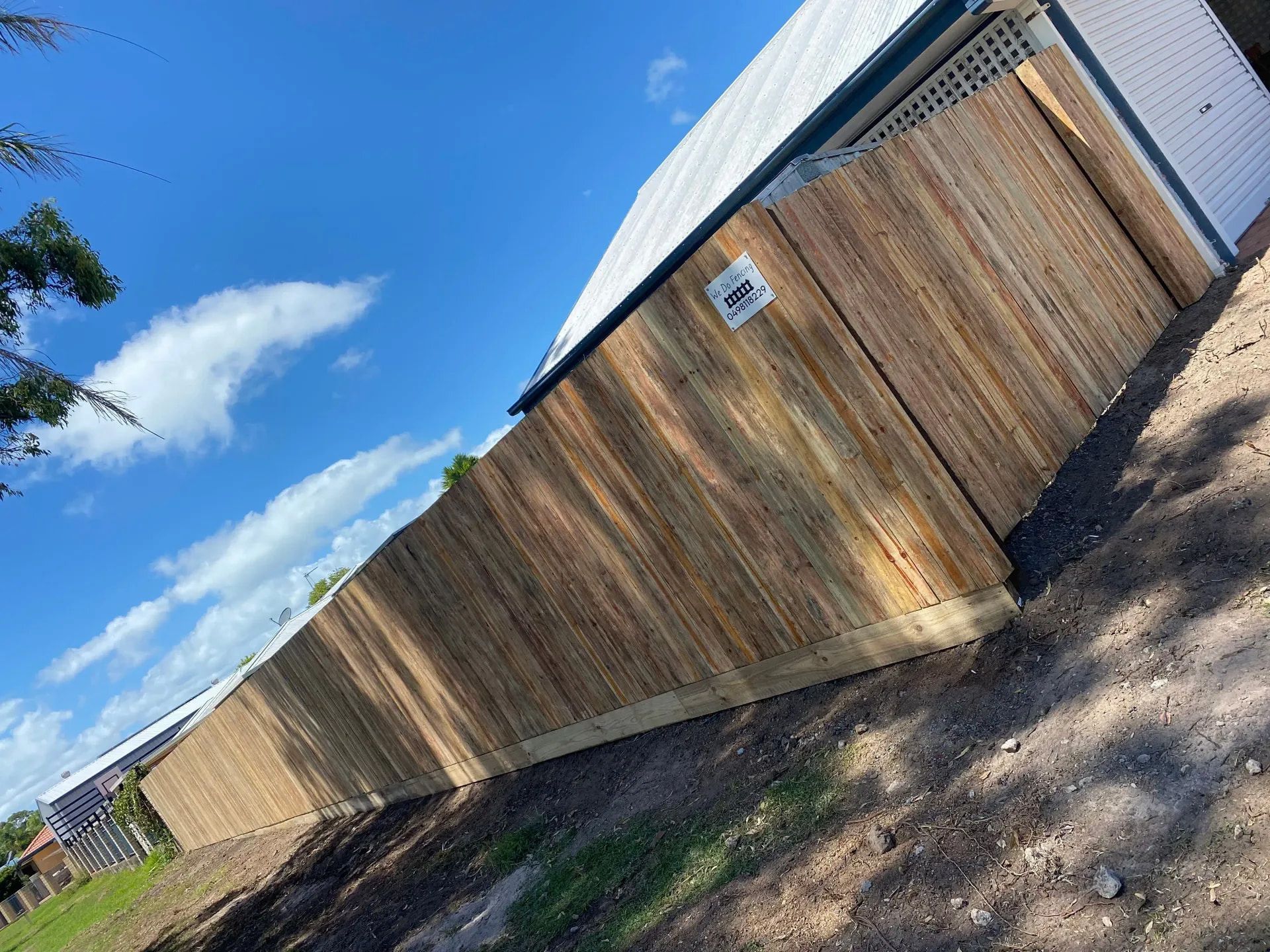 A Wooden Fence is Sitting in the Dirt in Front of a House — We Do Fencing in Sunshine Acres, QLD