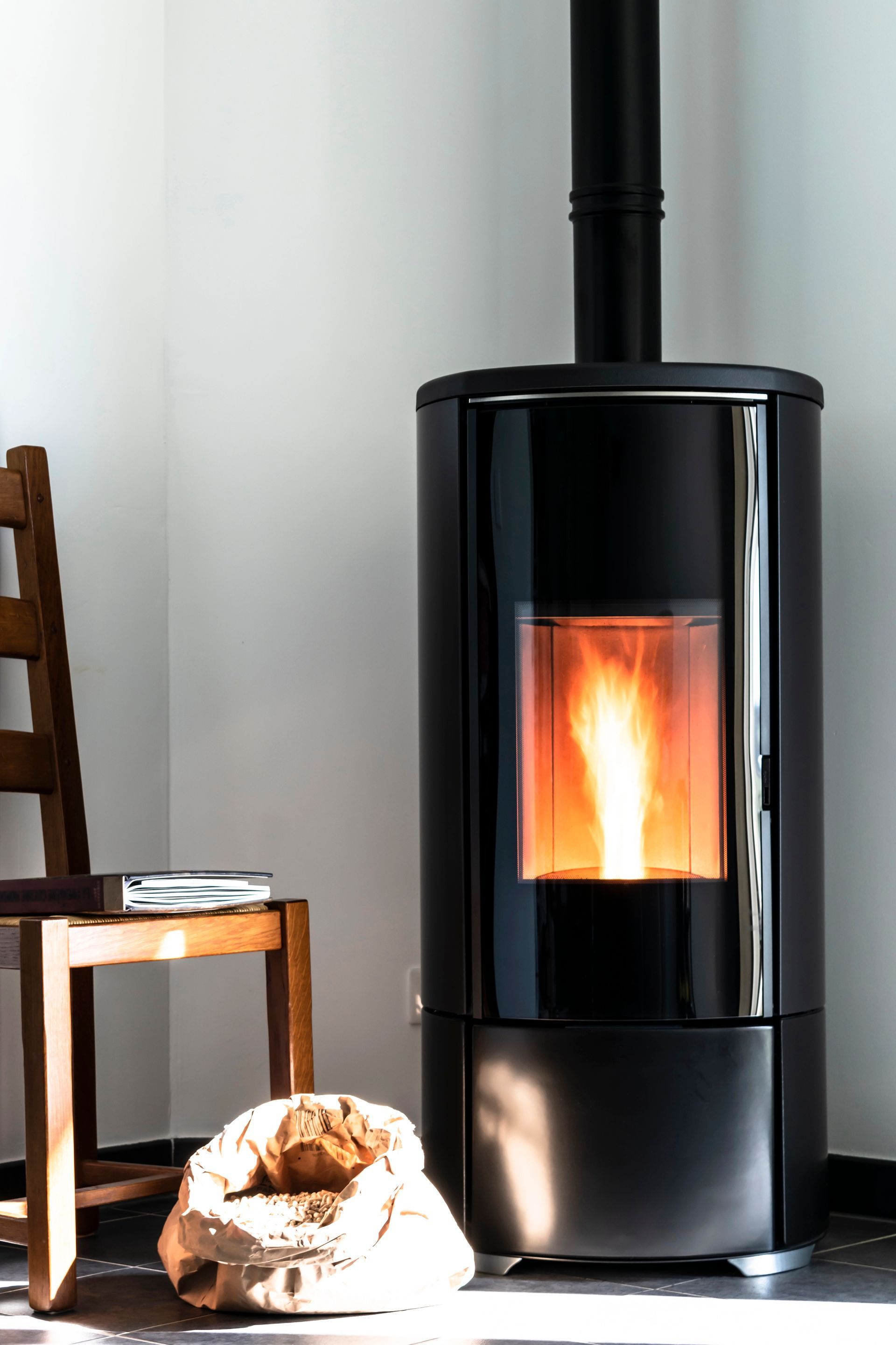 Stufa a pellet nera con fiamme, camino e una sedia.