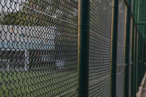 Green chain-link fence outdoors with blurred natural background. Green chain-link fence outdoors with blurred natural background.