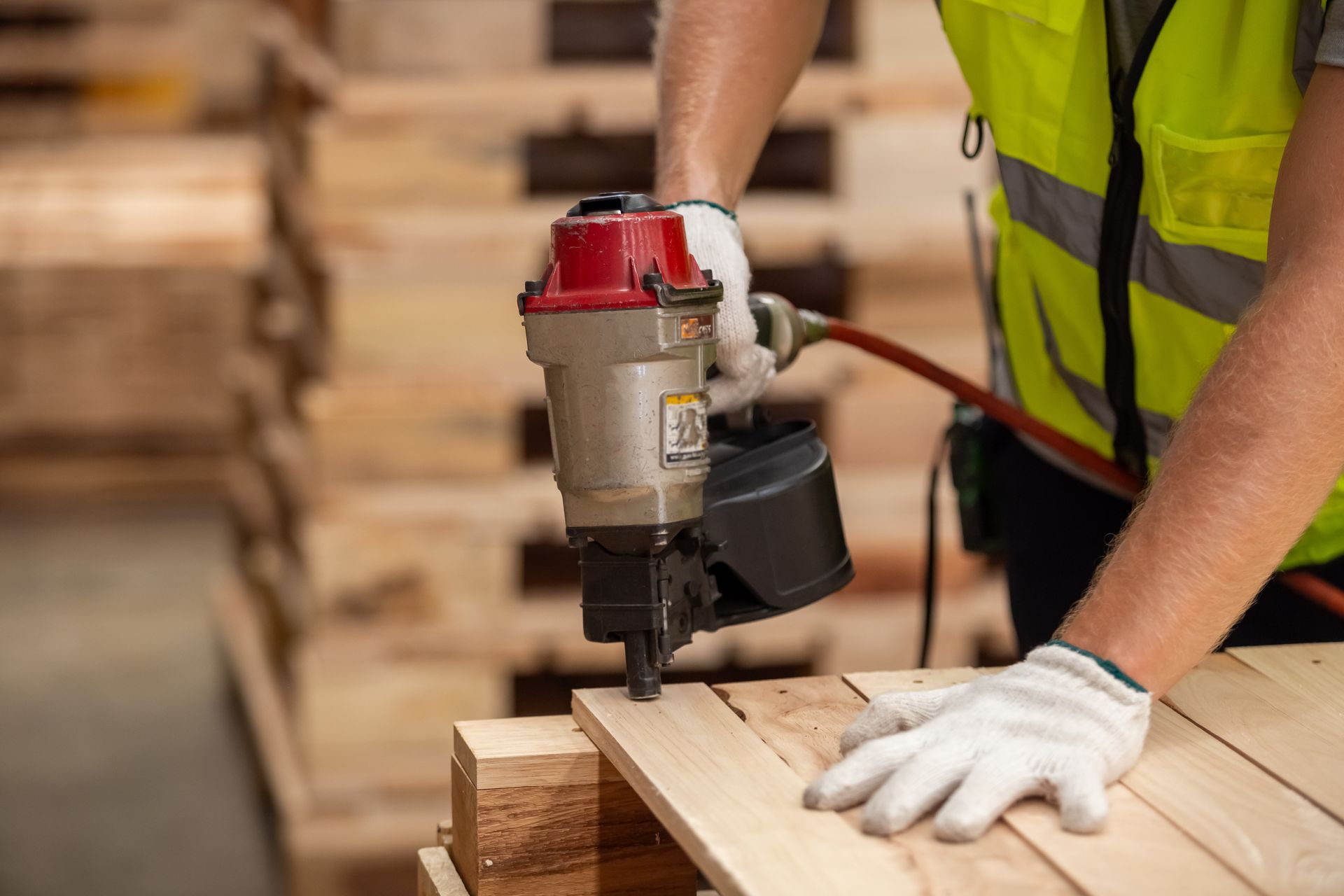 Person in safety vest using a pneumatic nail gun to assemble wooden pallet. Person in safety vest using a pneumatic nail gun to assemble wooden pallet.