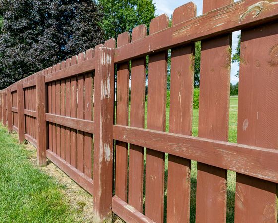 Weathered brown wooden fence along green yard with trees in background outdoor landscape scenic view.