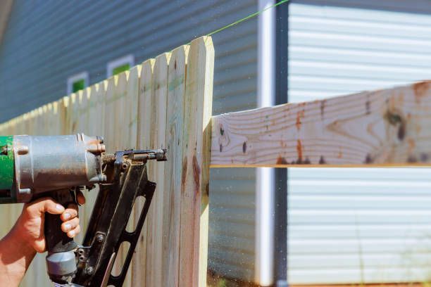 Fencing contractor builds sections of nailing a wooden fence around his yard.