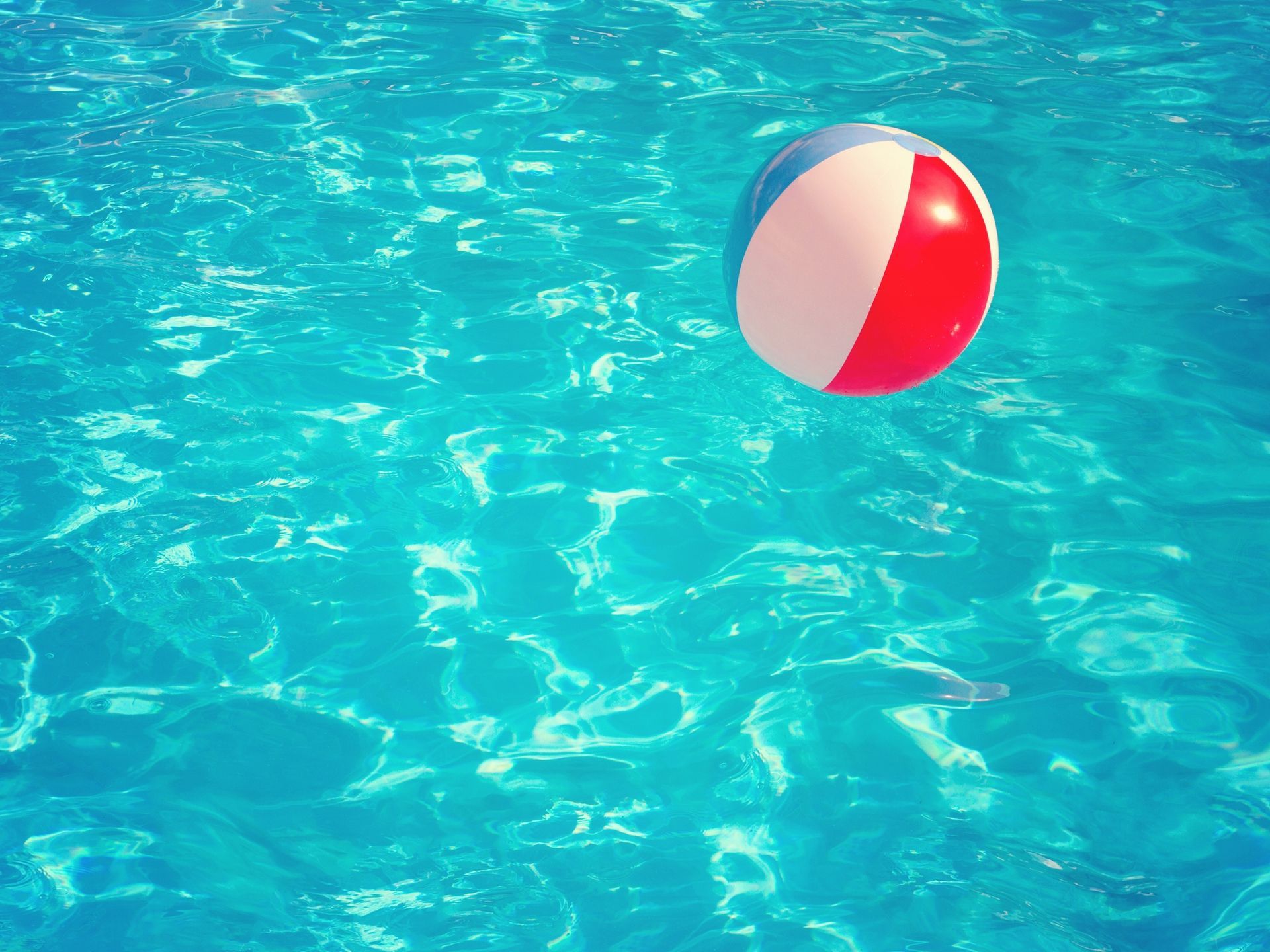 A red, white, and blue beach ball floating on calm, rippling turquoise water.