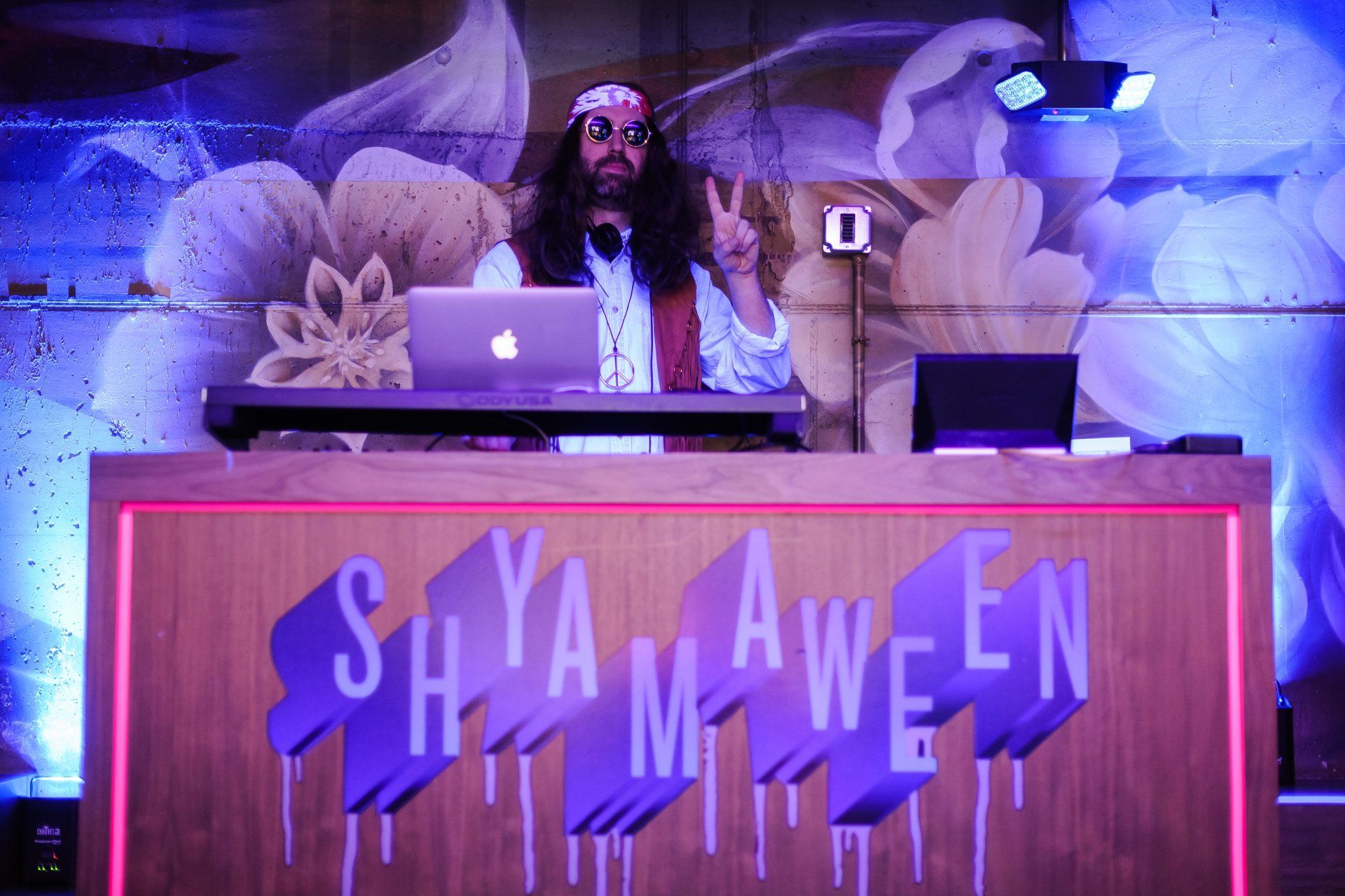 A man in a hippie costume is standing behind a dj booth.