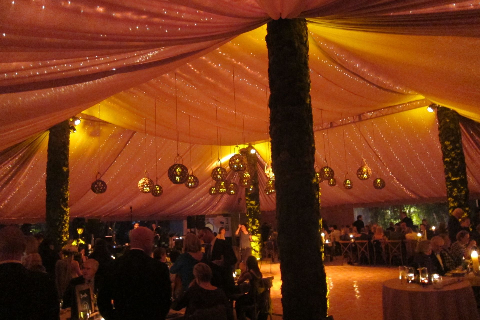 A group of people are sitting under a tent with lights hanging from the ceiling