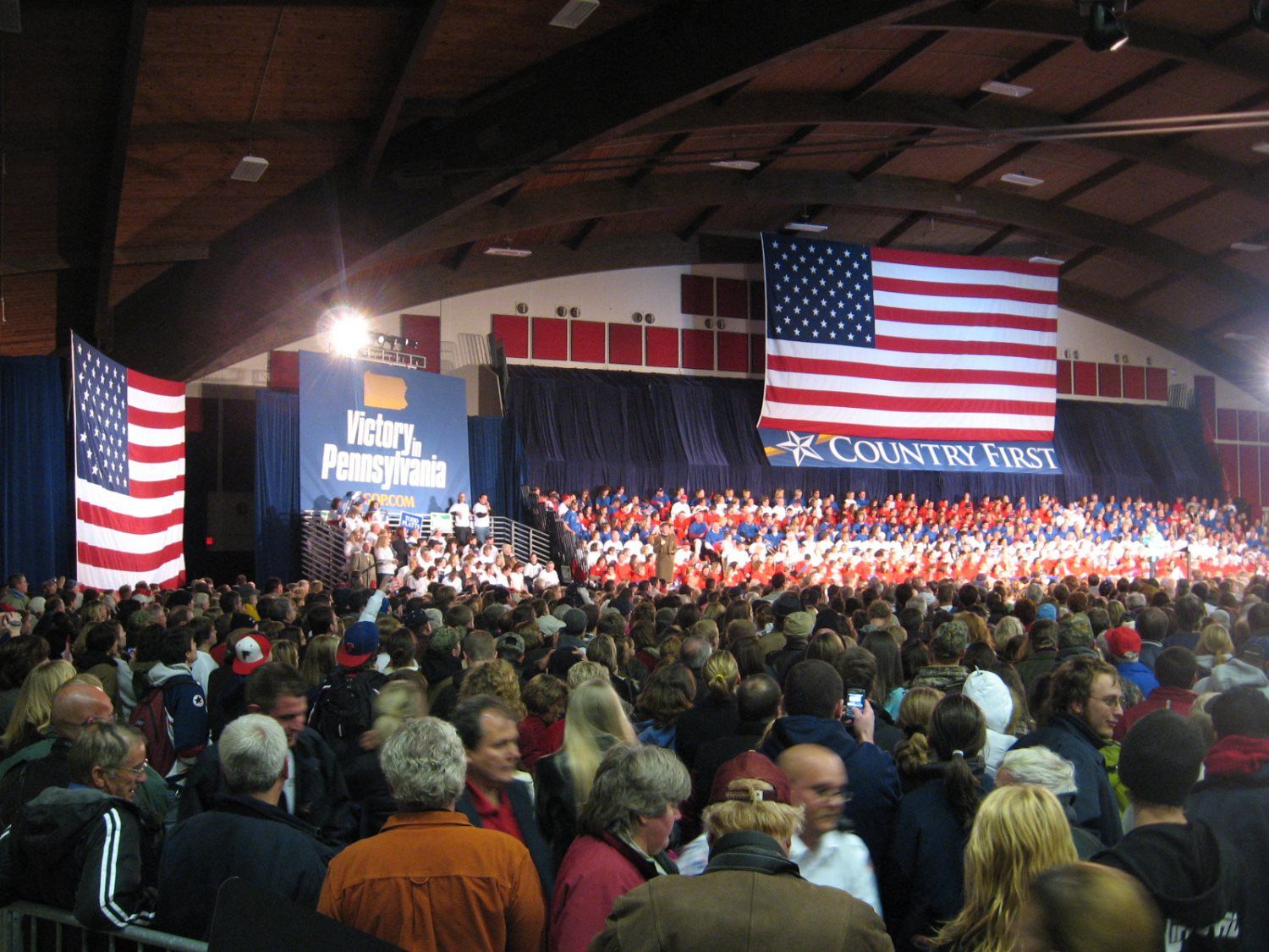 A large crowd of people are gathered in front of an american flag and a sign that says victory pennsylvania