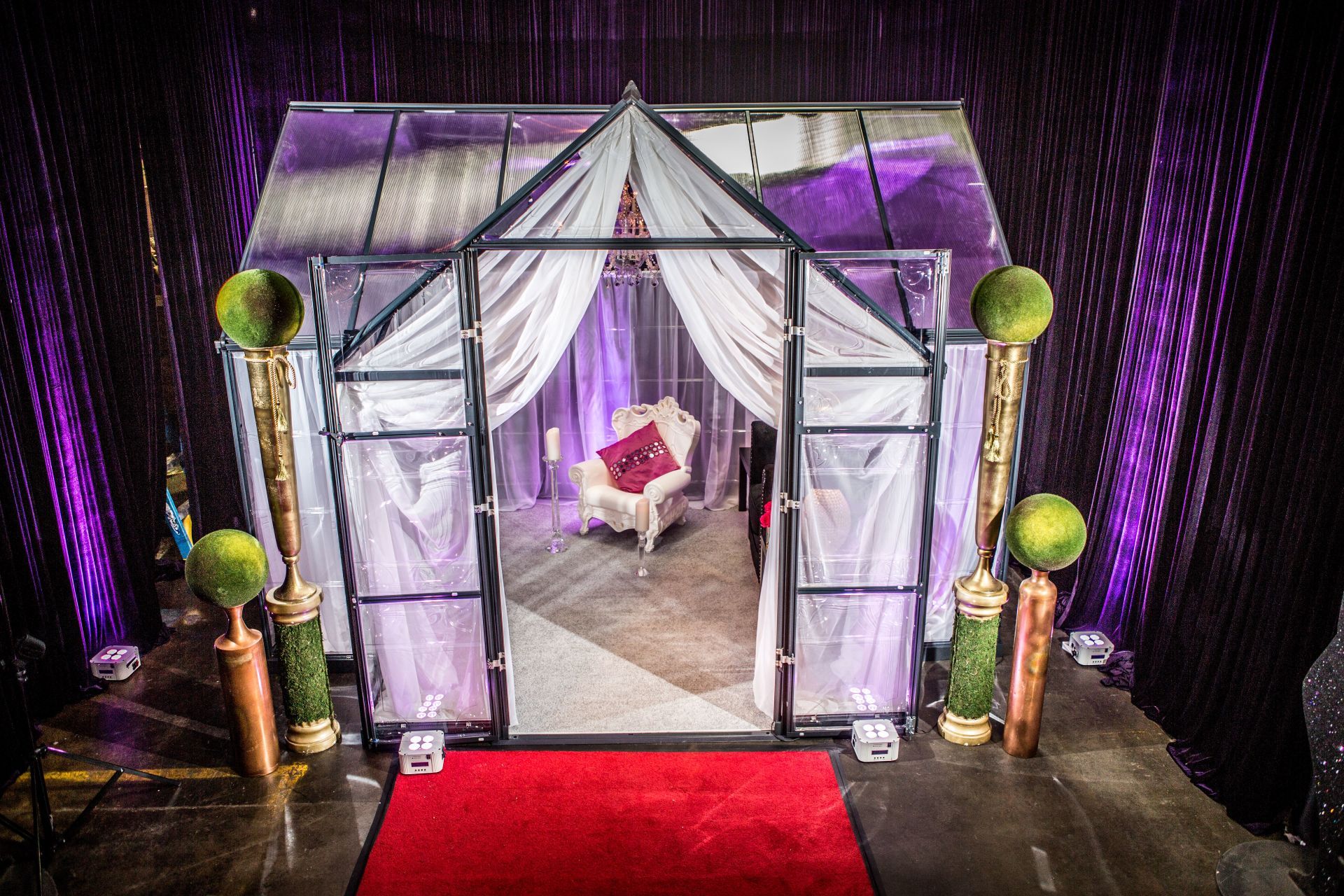 A red carpet is leading to a greenhouse with a chair inside of it.