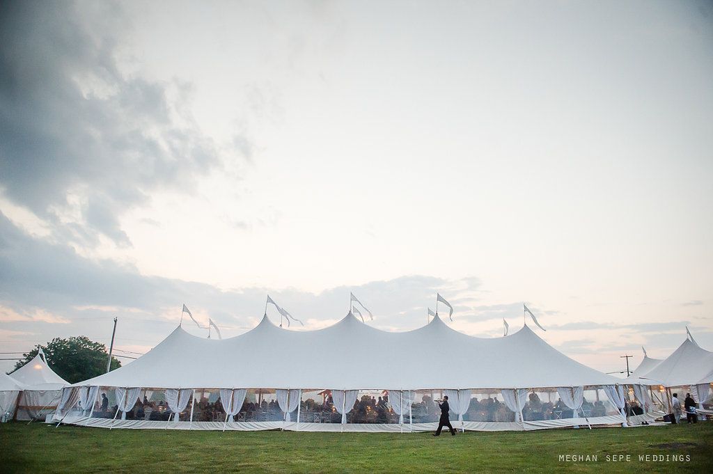 A large white tent is sitting in the middle of a grassy field.