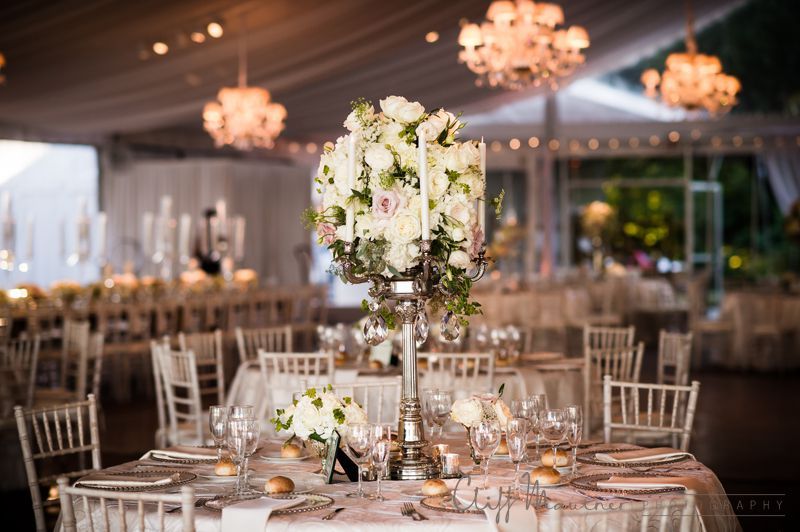 A table set for a wedding reception with a large vase of flowers on it.
