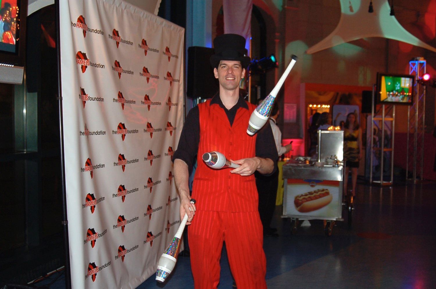 A man in a top hat is juggling two clubs