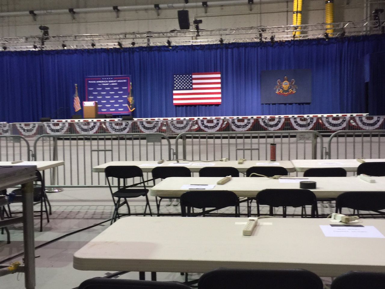 A classroom with tables and chairs and an american flag on the stage