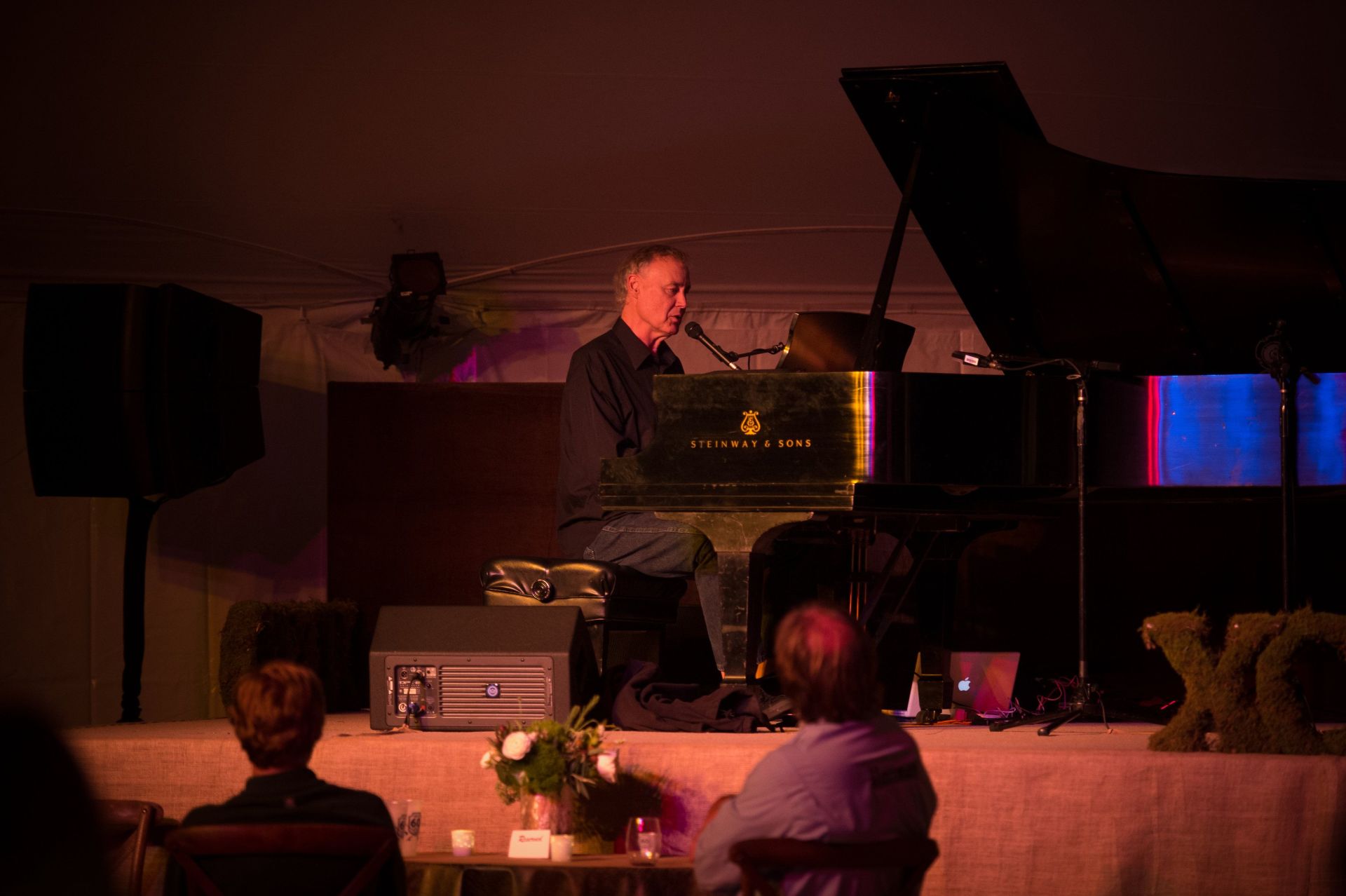 A man is playing a piano on a stage and singing into a microphone.