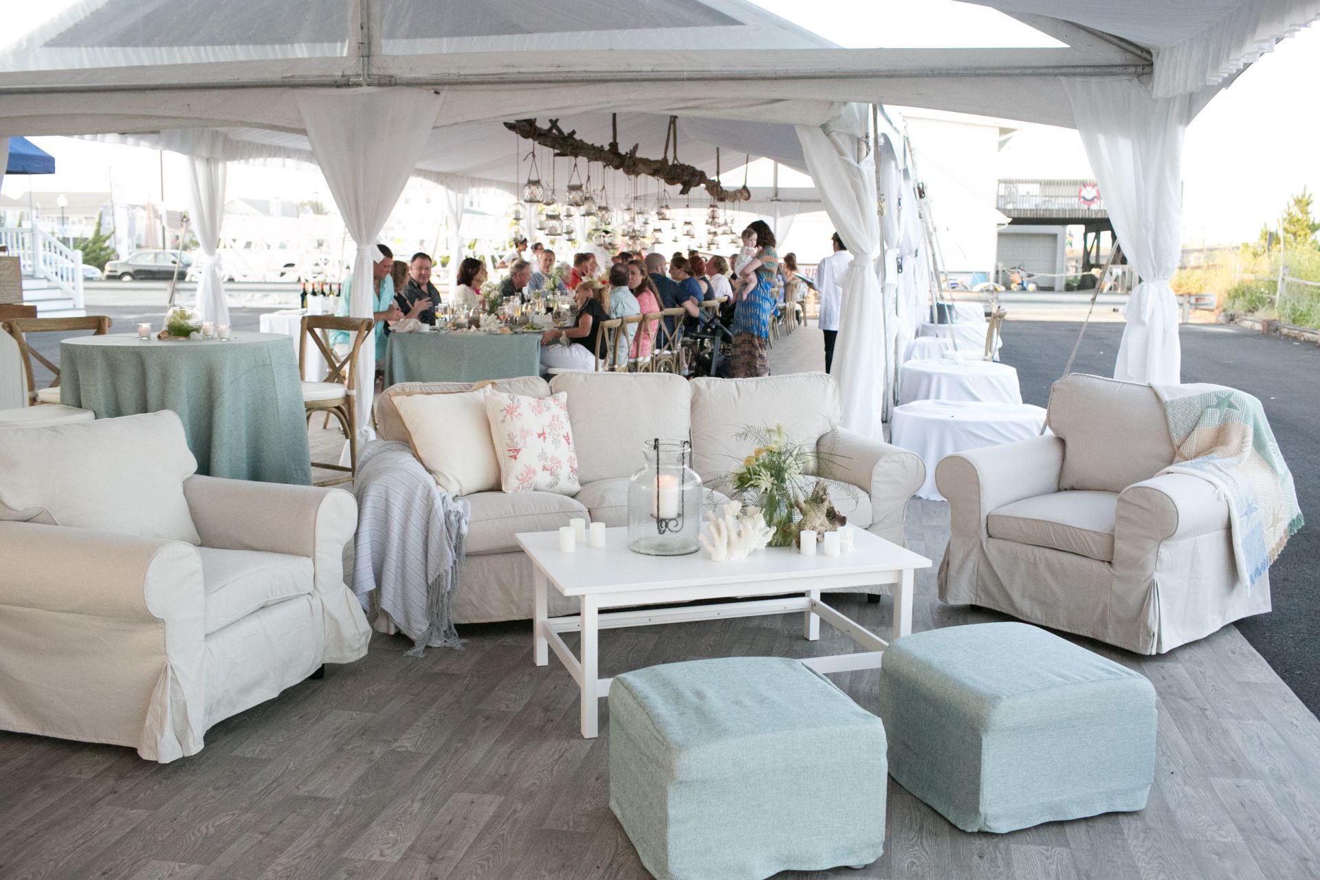 A group of people are sitting under a tent with white furniture