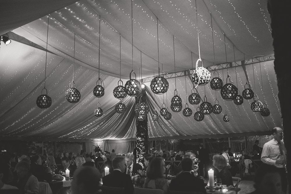 A group of people are sitting at tables under a tent with lights hanging from the ceiling.