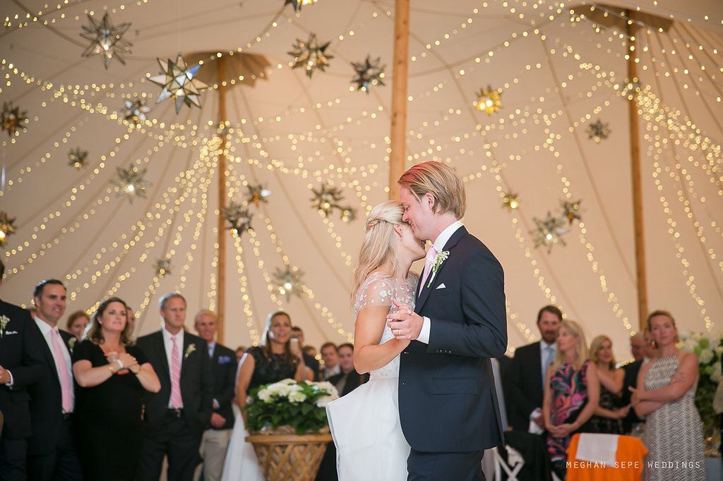 A bride and groom are kissing during their first dance in a tent.