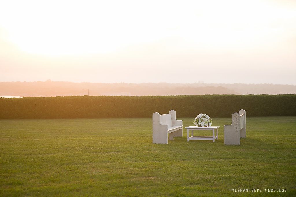 A group of white chairs and a table in a grassy field at sunset.