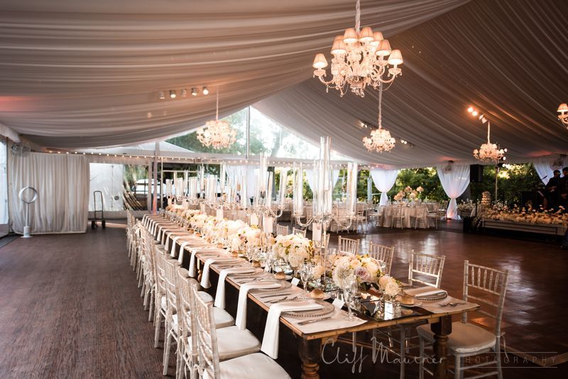 A long table and chairs in a tent with chandeliers hanging from the ceiling.