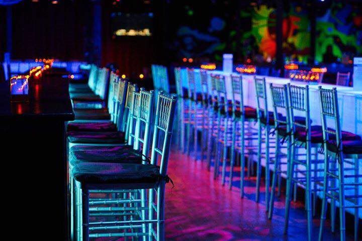 A row of bar stools in a dark room with glow in the dark lights.