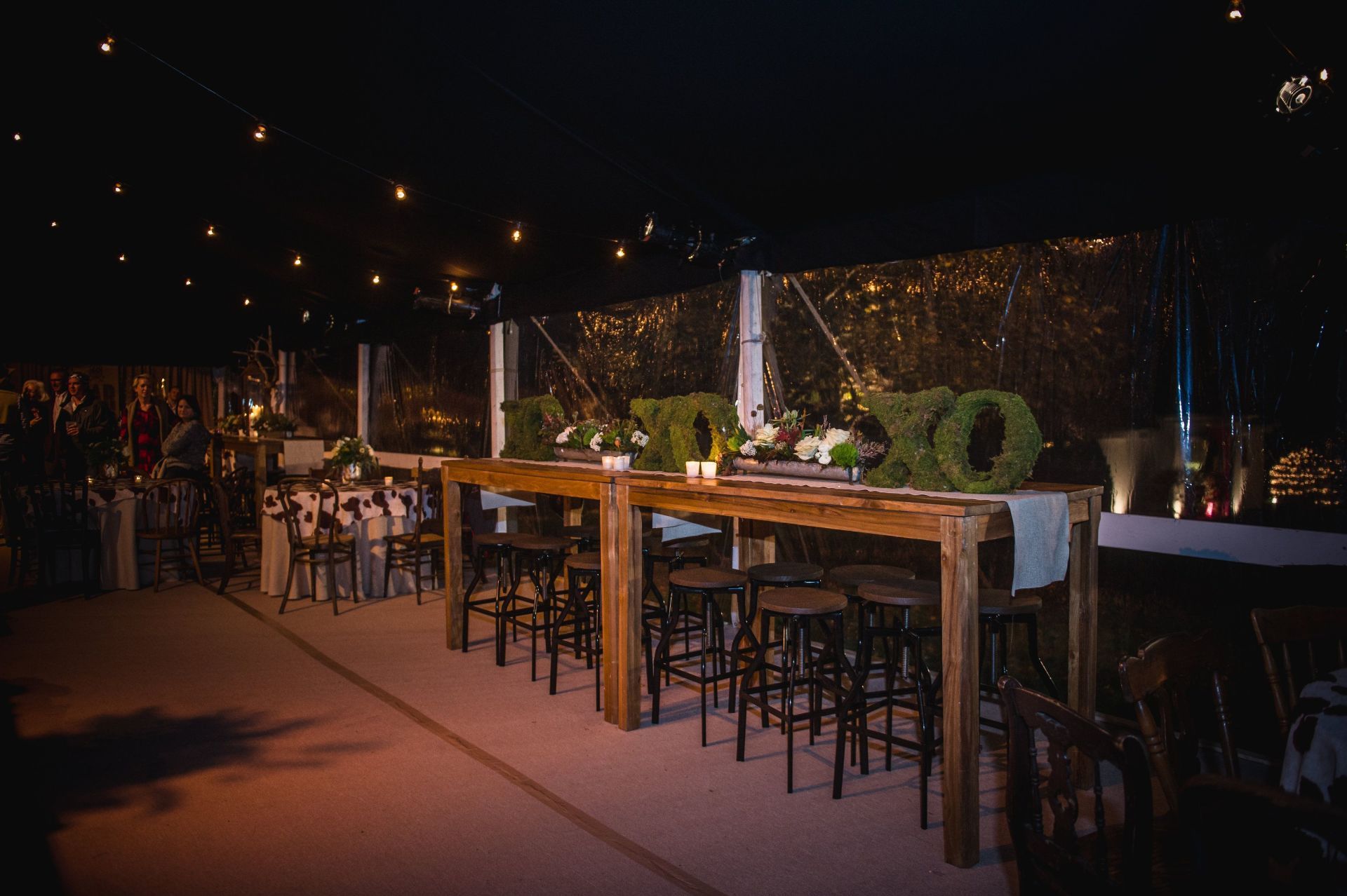 A row of wooden tables and chairs under a tent at night.