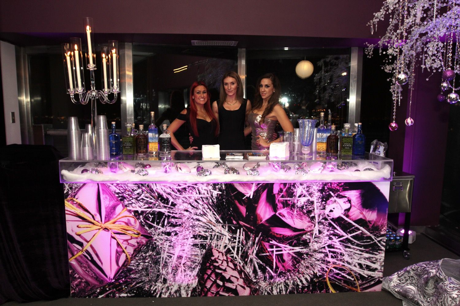 Three women are standing in front of a purple bar.