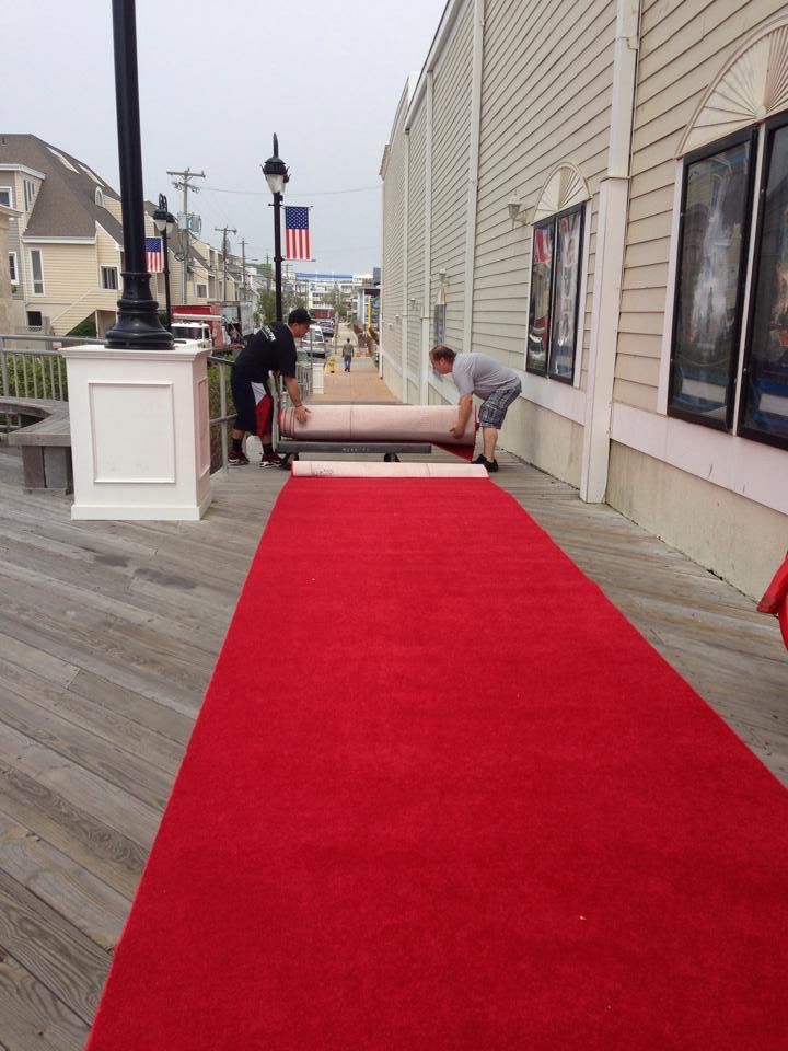 Two men are working on a red carpet outside of a building