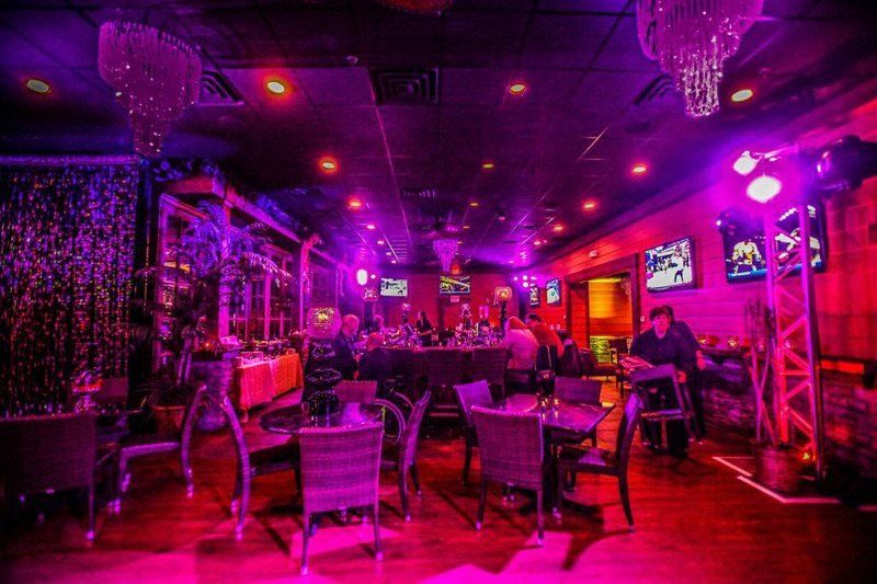 A group of people are sitting at tables in a dark room with purple lights.