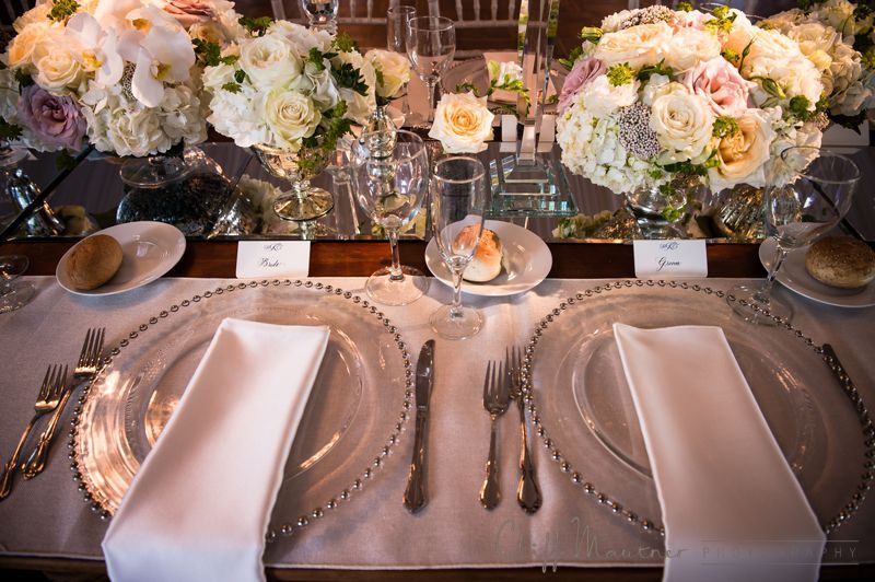 A table set for a wedding reception with plates , silverware , and flowers.