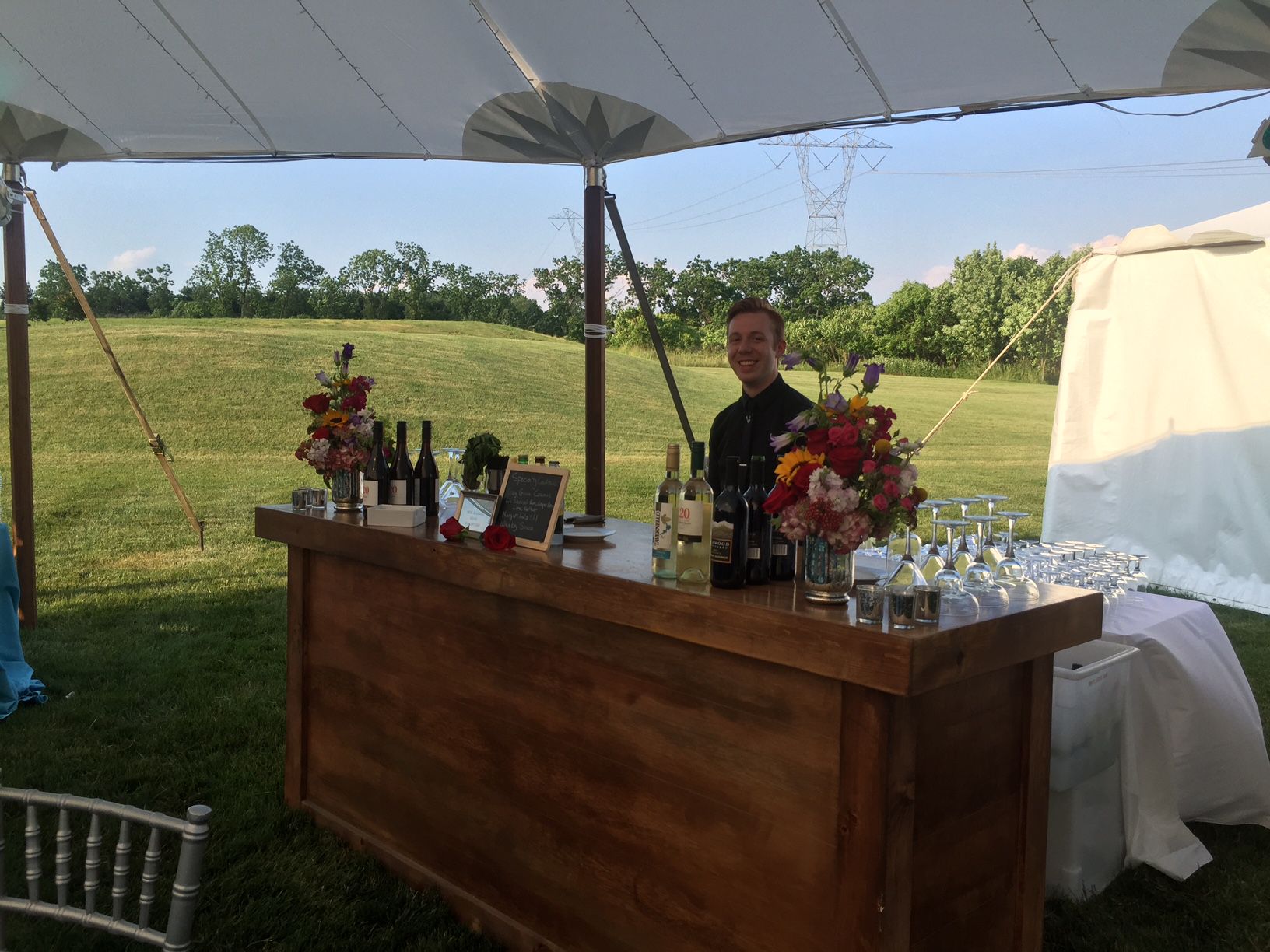 A man is standing behind a wooden bar under a tent.