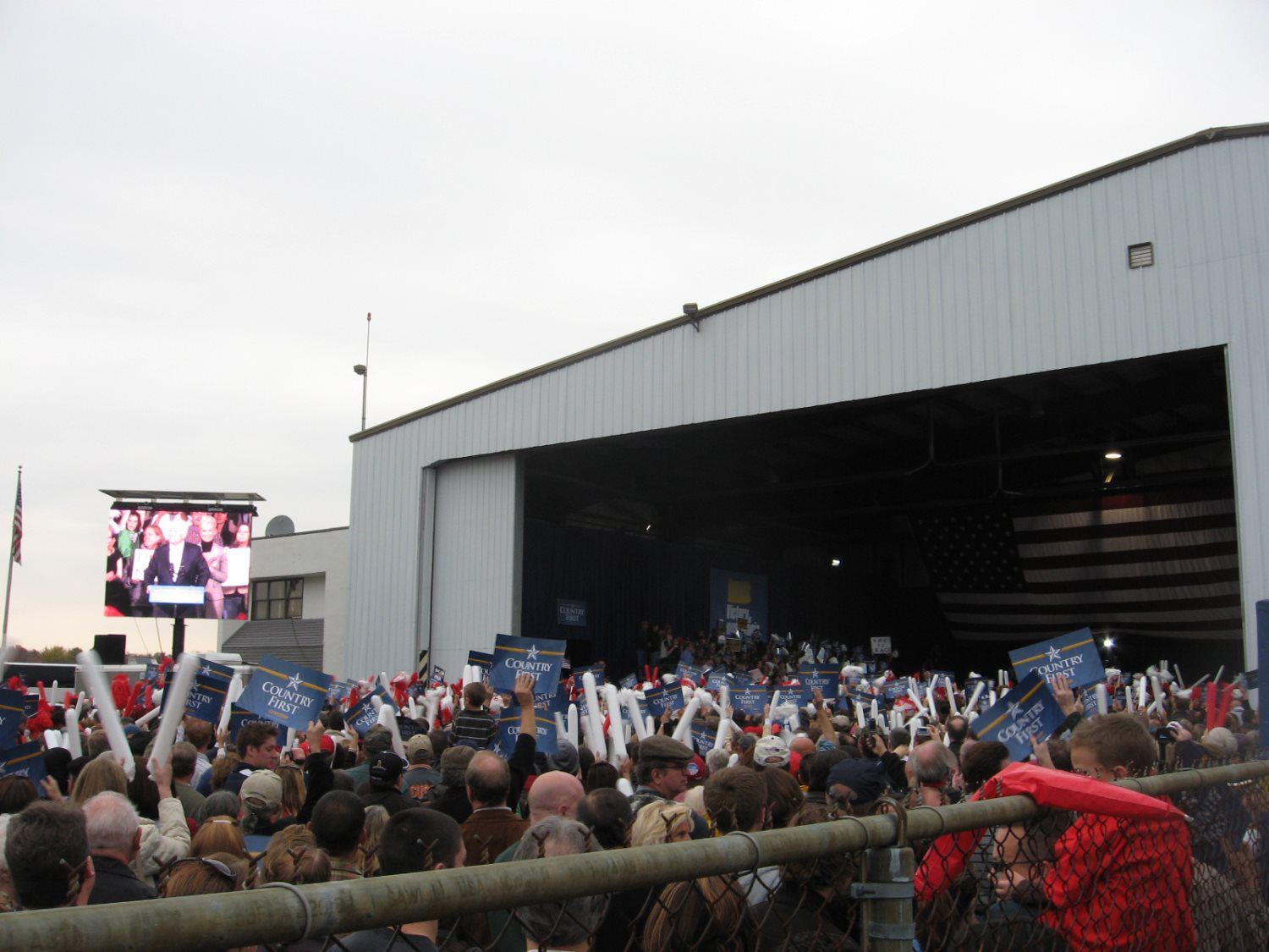 A large crowd of people are gathered in front of an airplane hangar