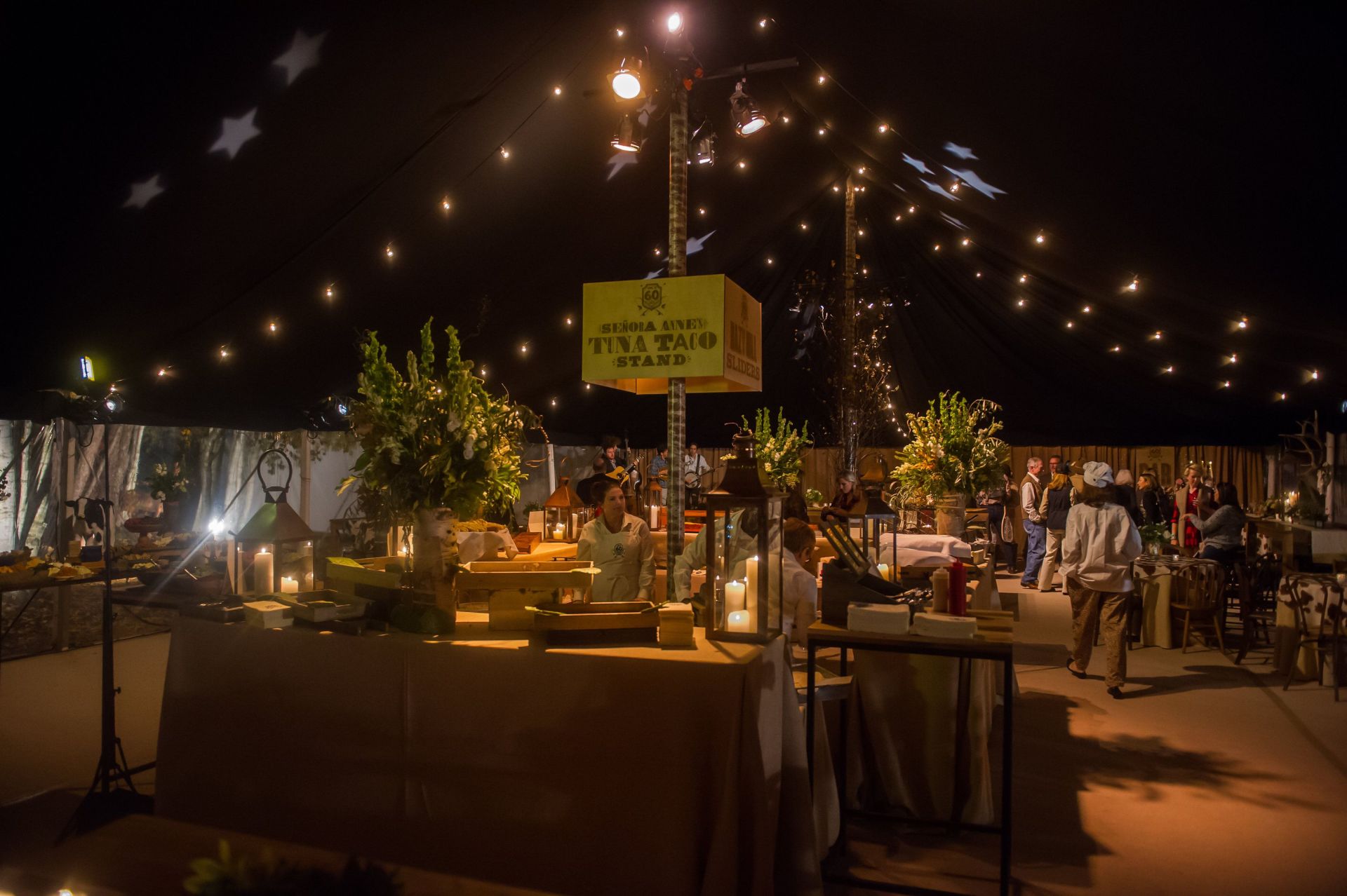 A group of people are standing around a table in a tent at night.