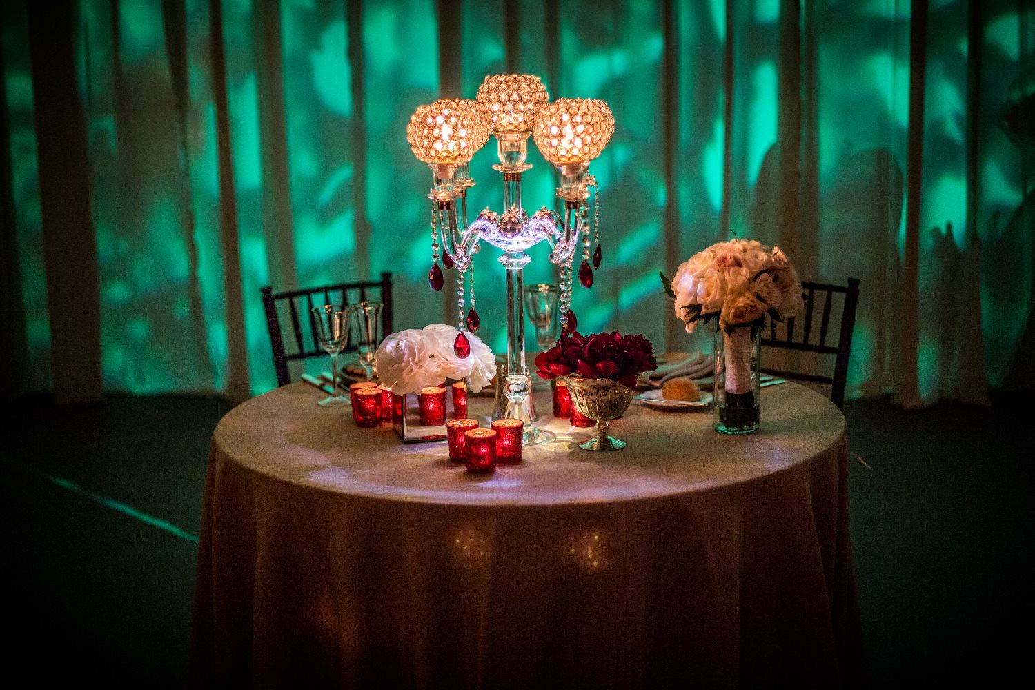 A table with candles and flowers on it in front of a green curtain.