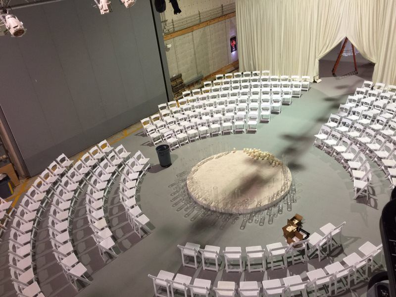 A large auditorium with rows of white chairs arranged in a circle.