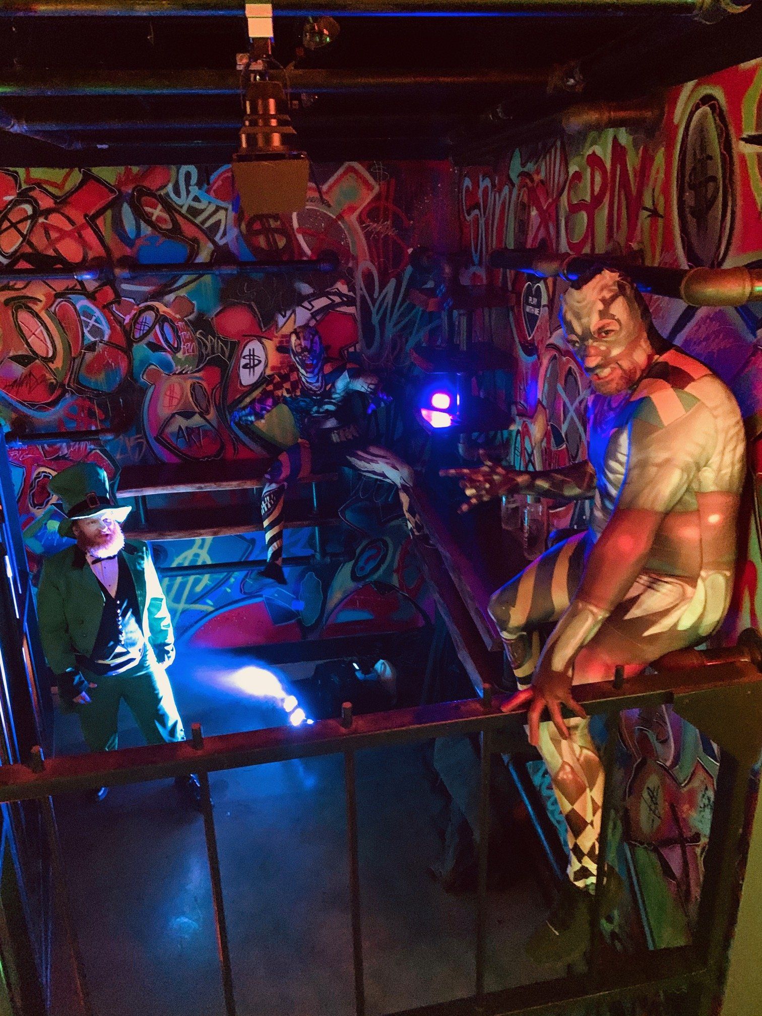 A man in a green hat is standing in front of a graffiti covered wall.