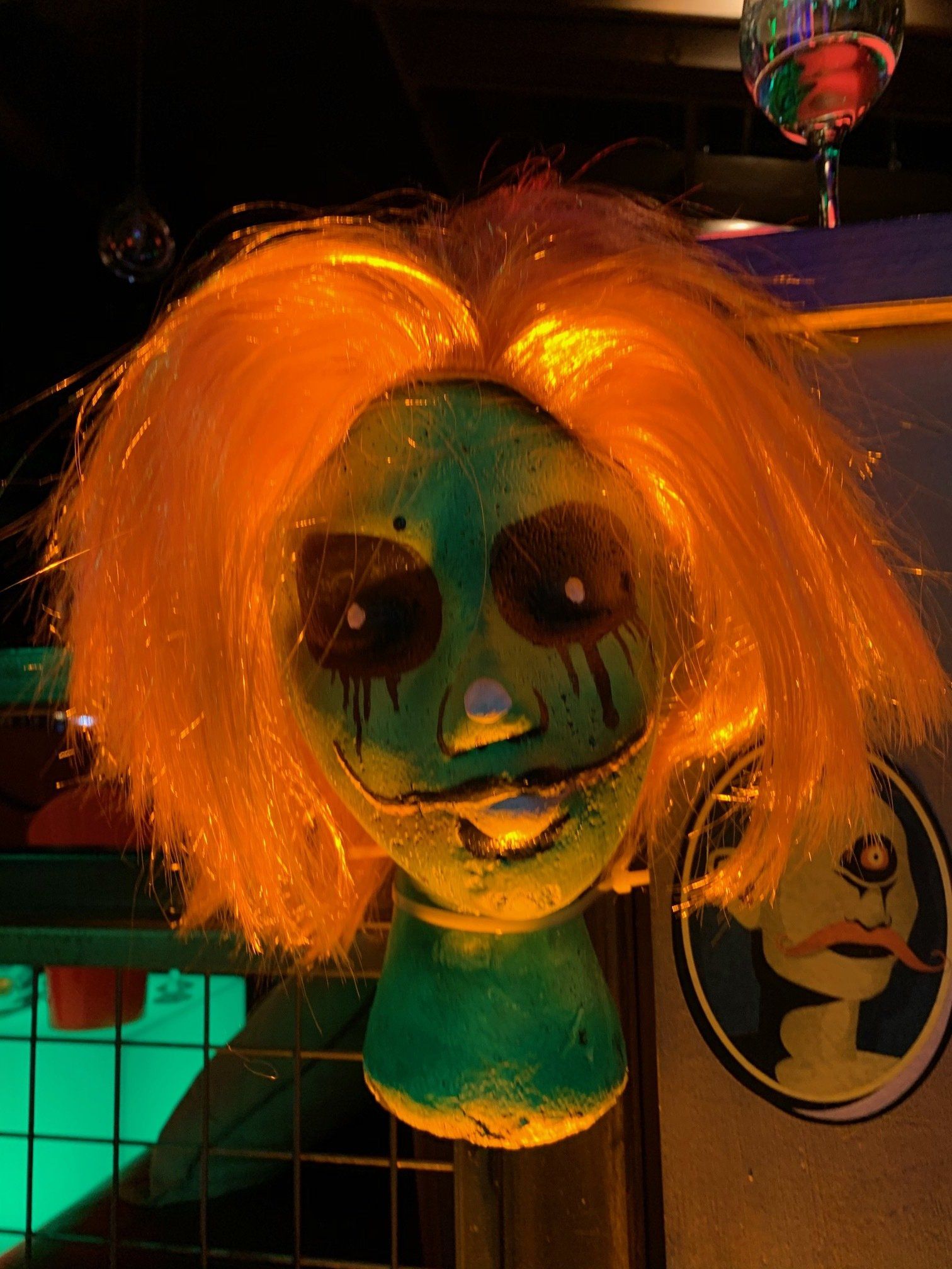 A mannequin head with a green face and orange hair.