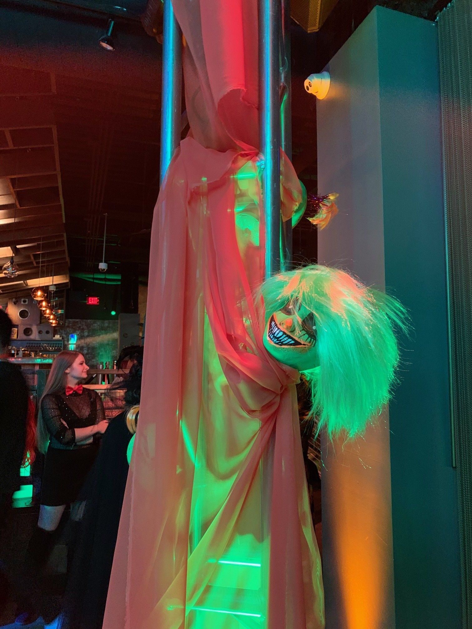 A clown is hanging from a pole in a dark room.