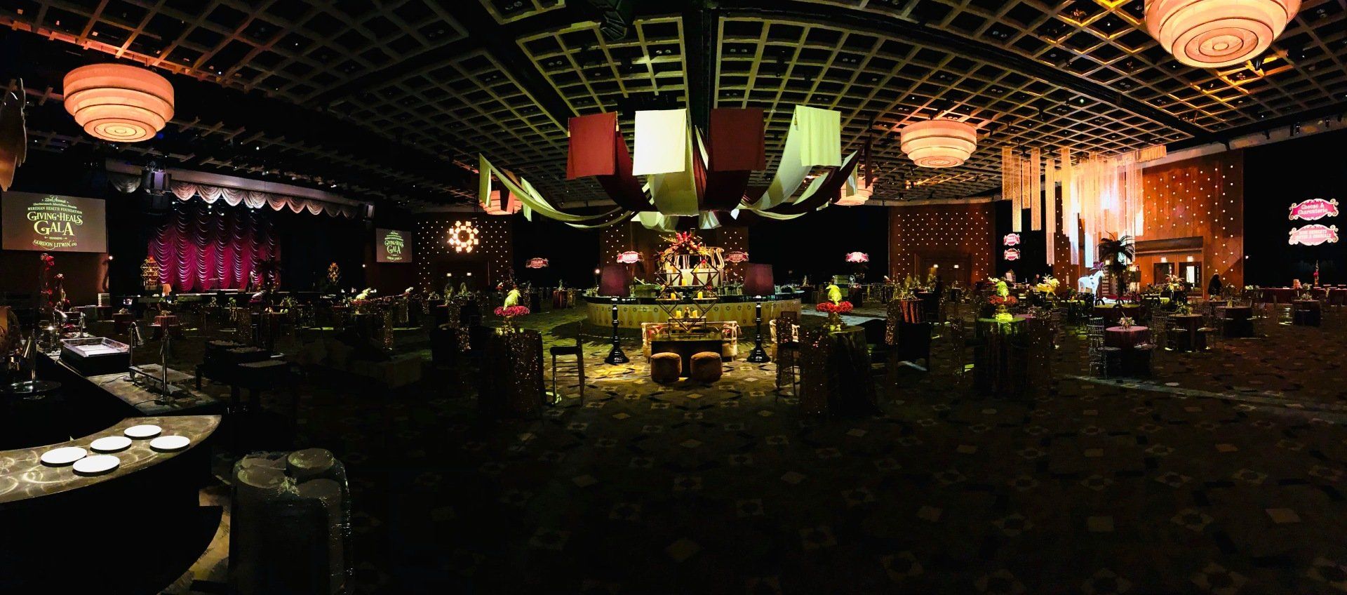 A large room with tables and chairs and a stage in the background.