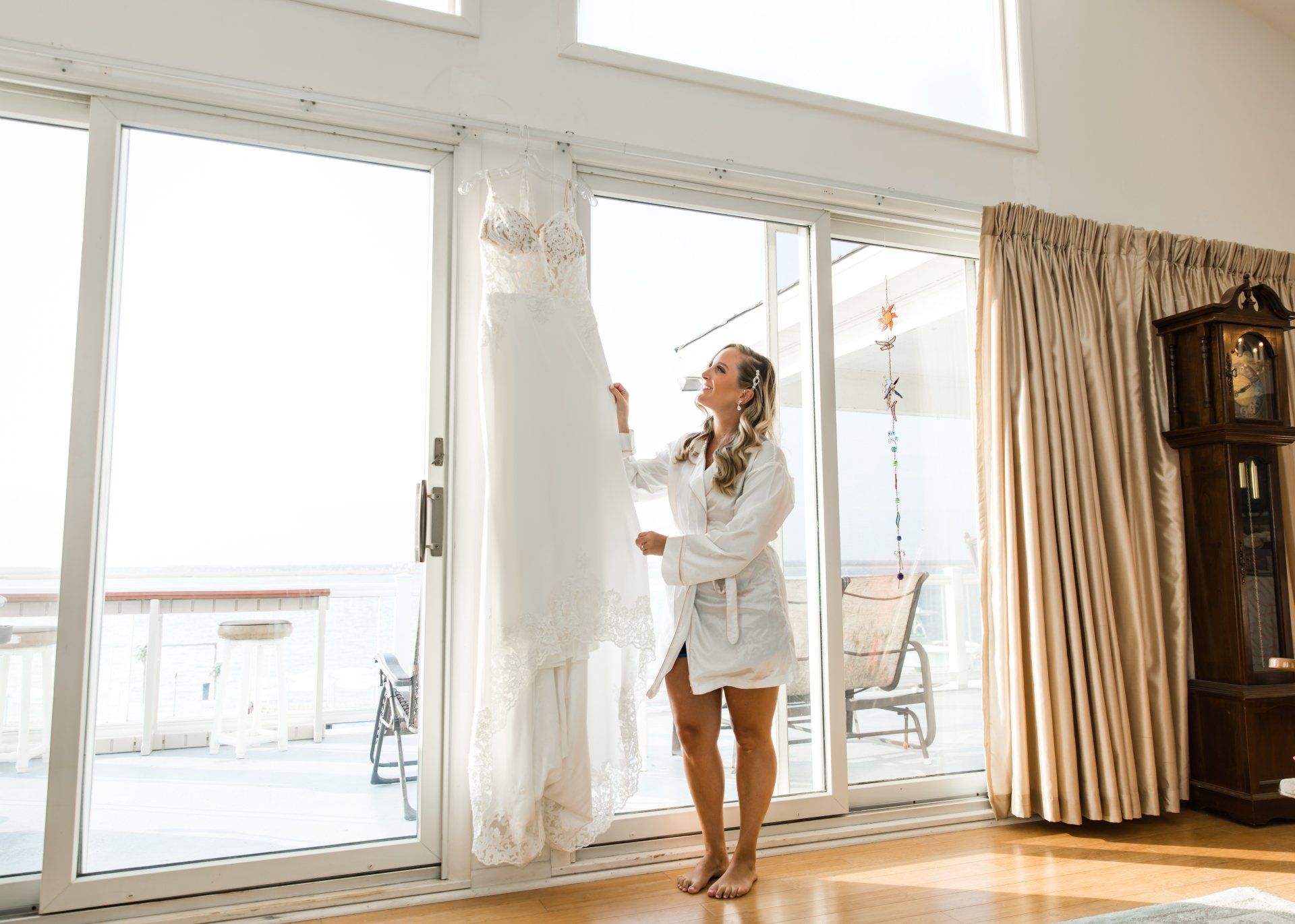 A woman is standing in front of a window holding a wedding dress.