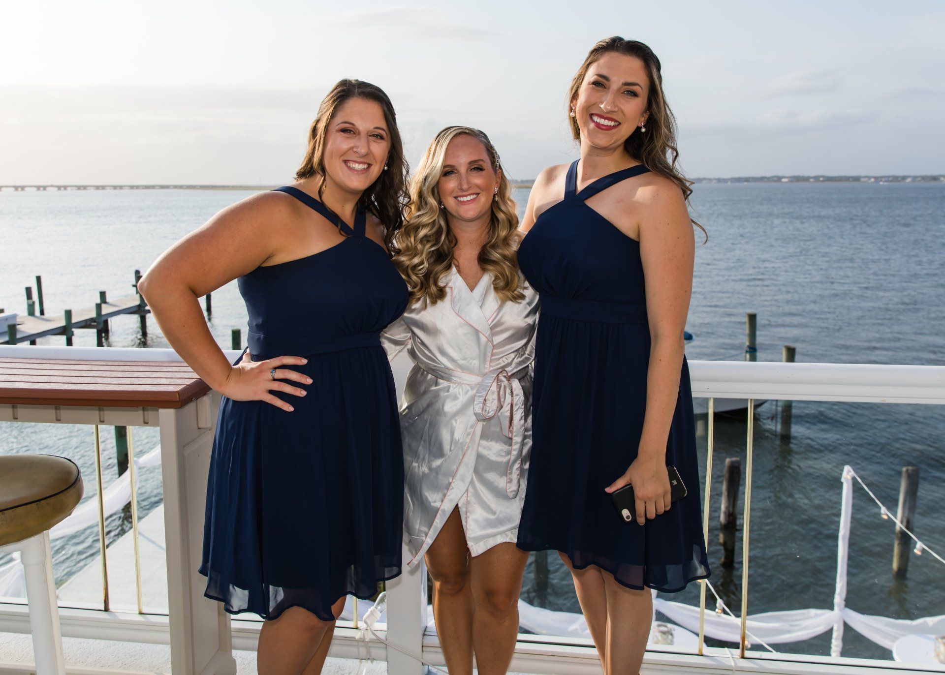 A bride and her bridesmaids are posing for a picture on a balcony overlooking the ocean.