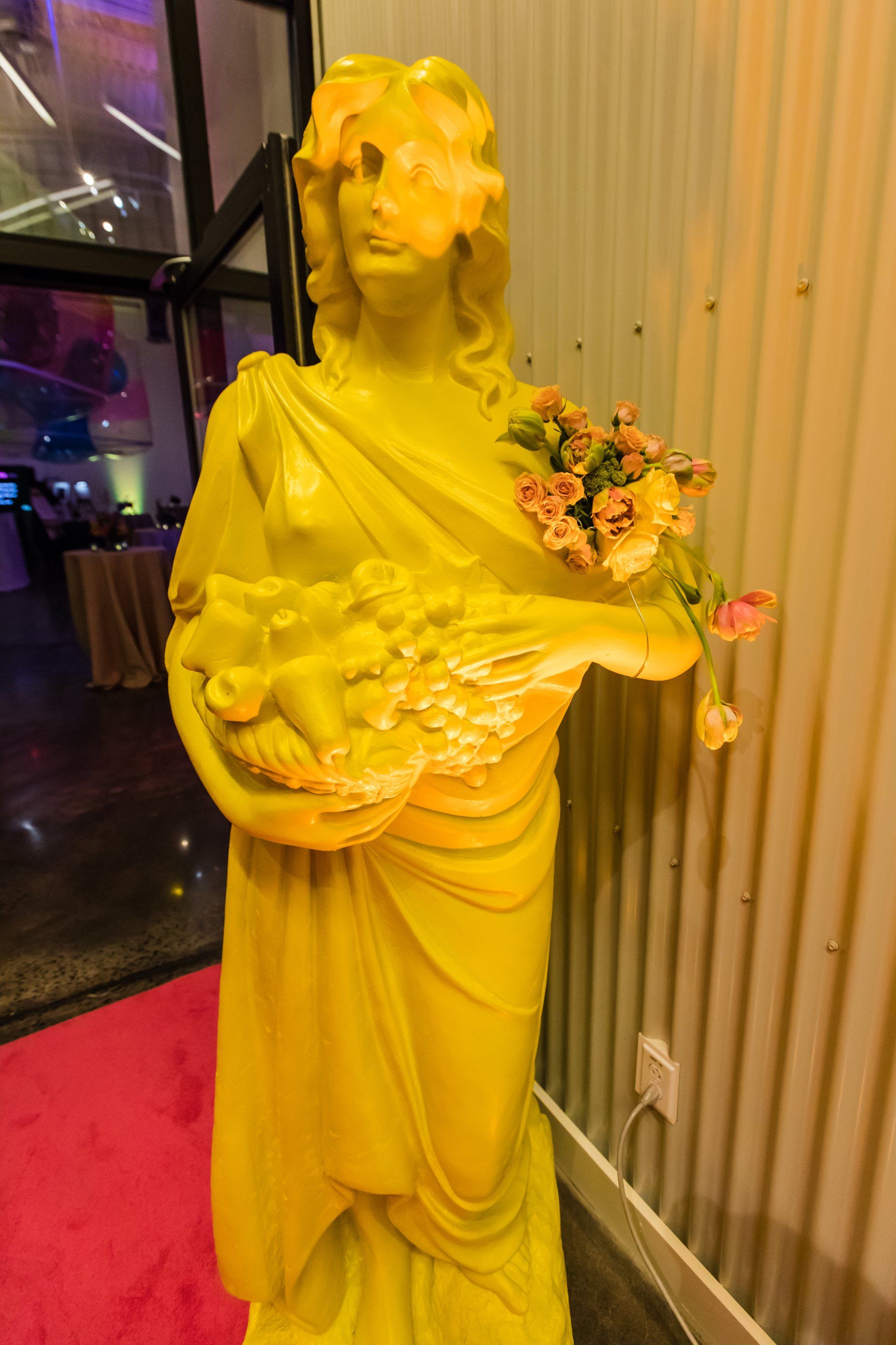 A yellow statue of a woman holding a vase of flowers.
