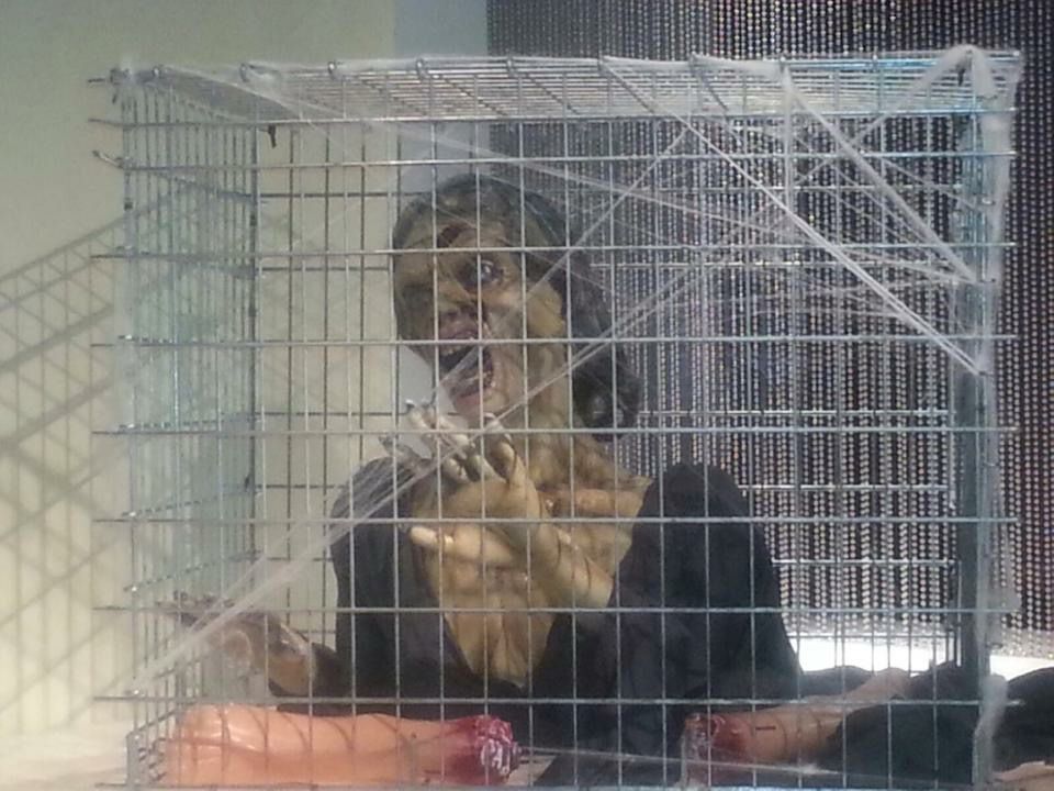 A zombie is sitting in a cage with a doll.