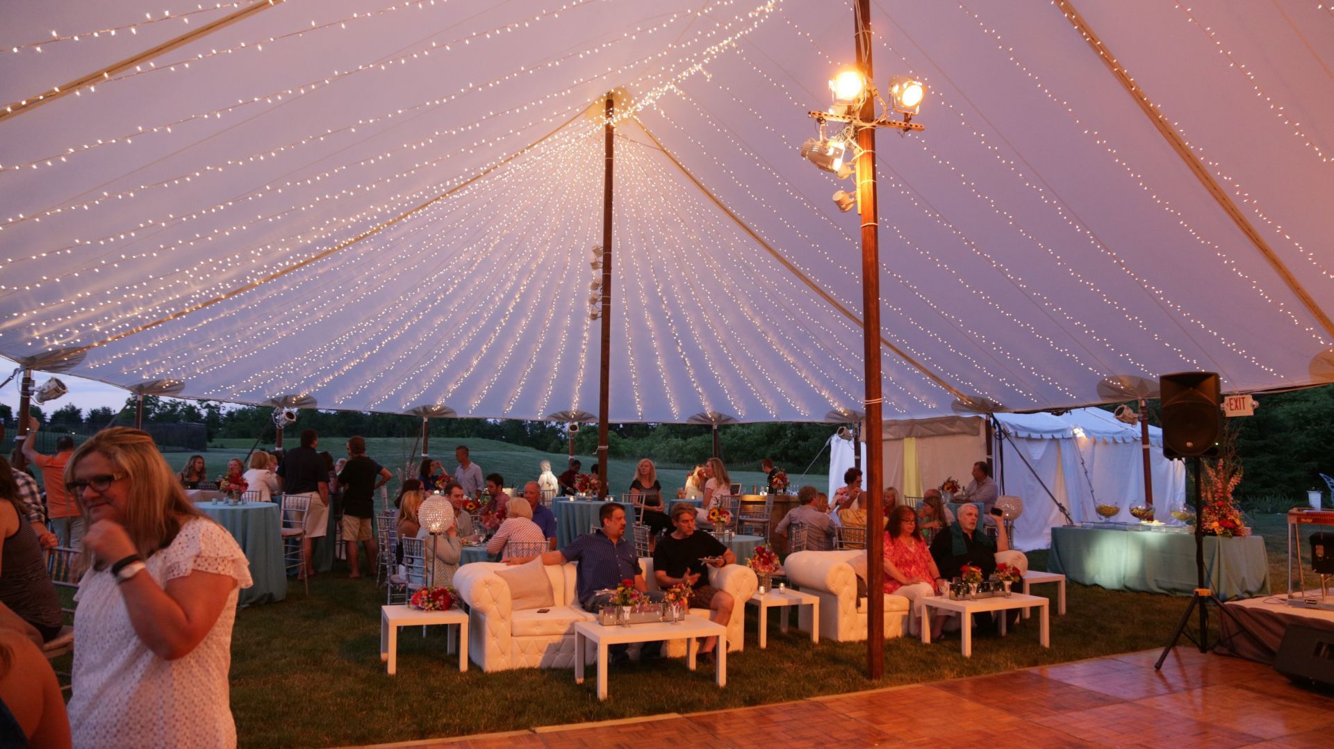 A group of people are sitting under a tent at a party.