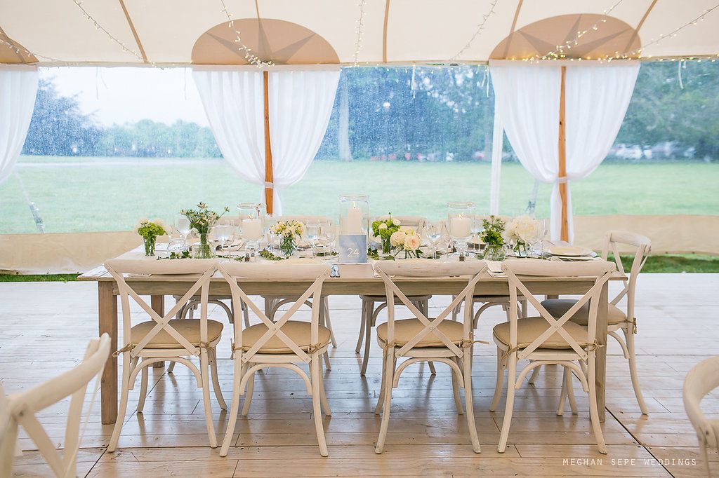 A long table and chairs under a tent with a field in the background.