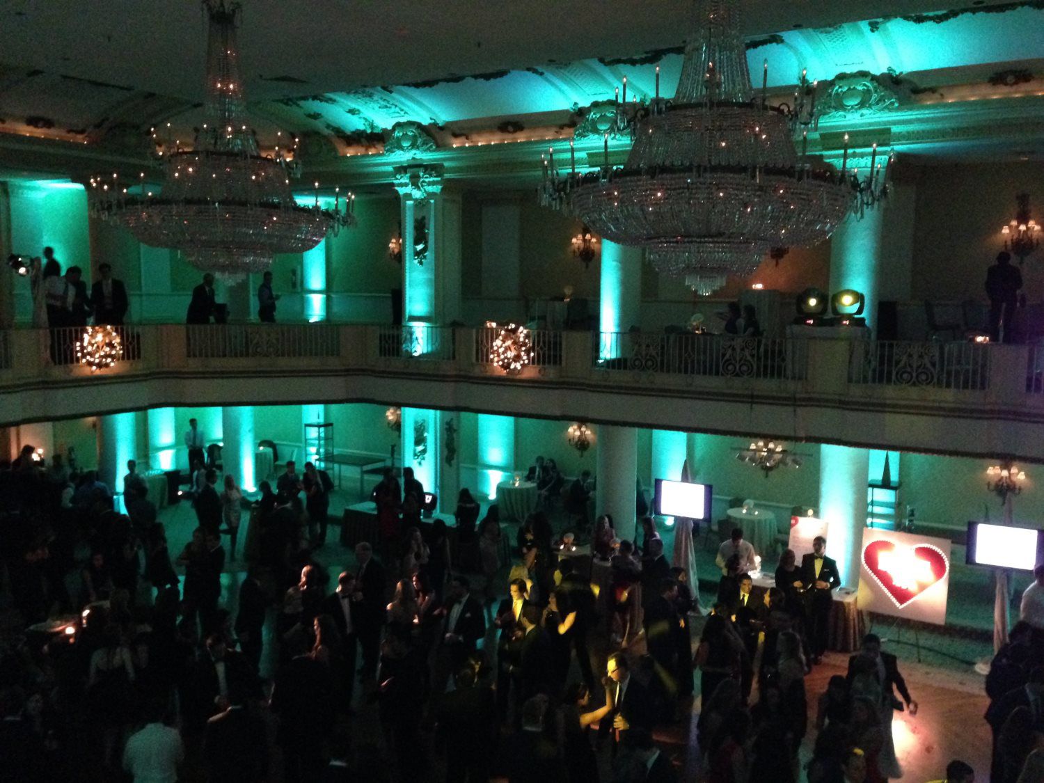 A crowd of people are gathered in a large room with green lights