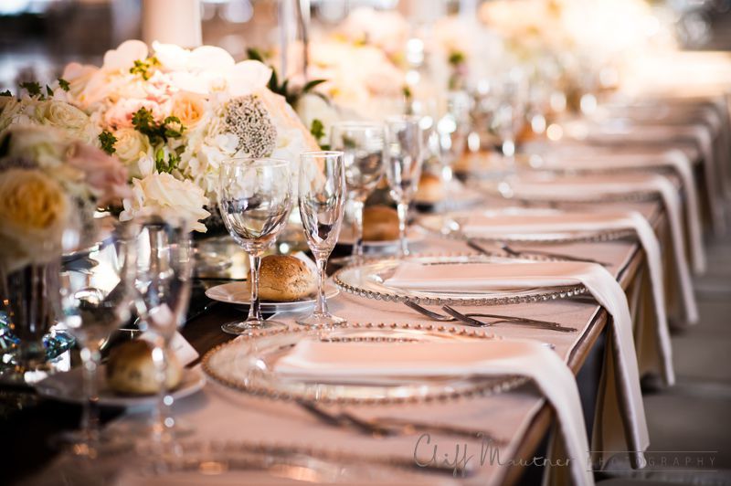 A long table set for a wedding reception with plates , glasses , and flowers.