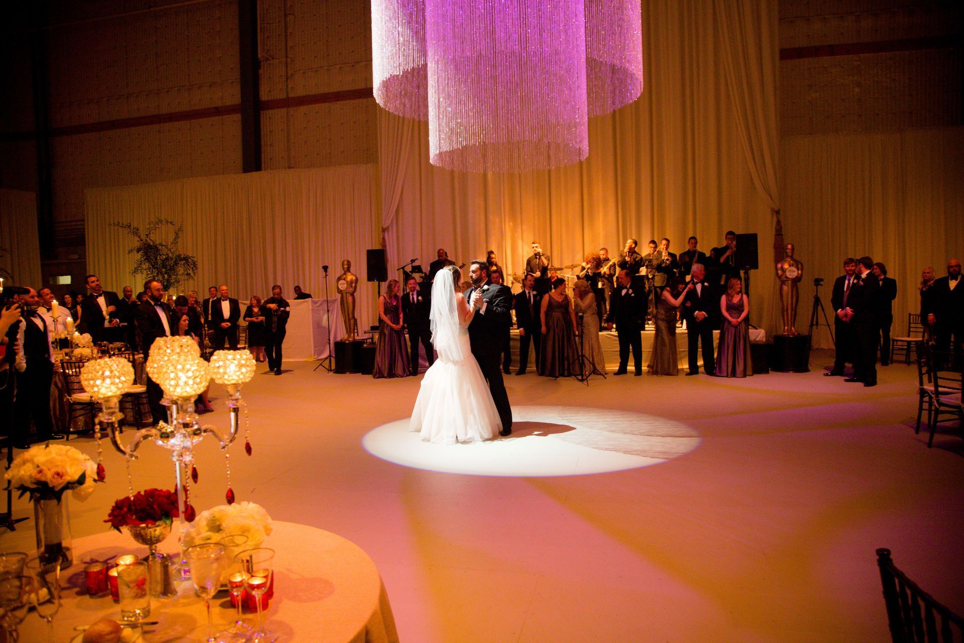 A bride and groom are dancing at their wedding reception under a purple chandelier.