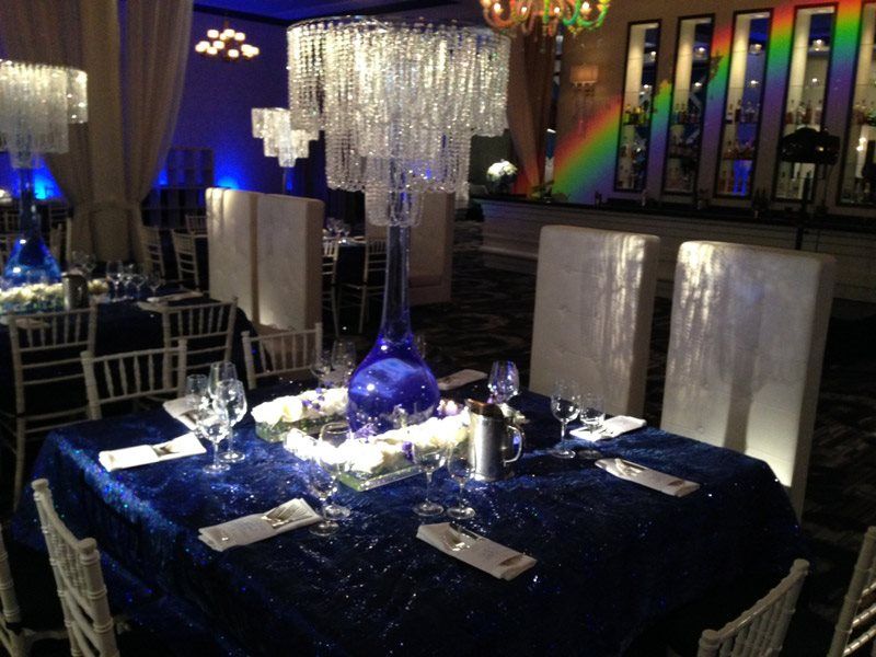 A table set for a party with a blue table cloth and white chairs.