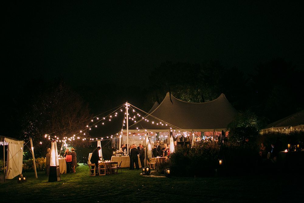 A group of people are standing outside of a tent at night.